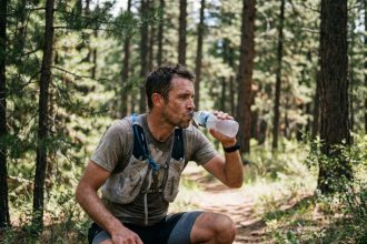 Coureur de trail s'hydratant avec une boisson électrolytique sur un sentier forestier pendant un effort d'endurance